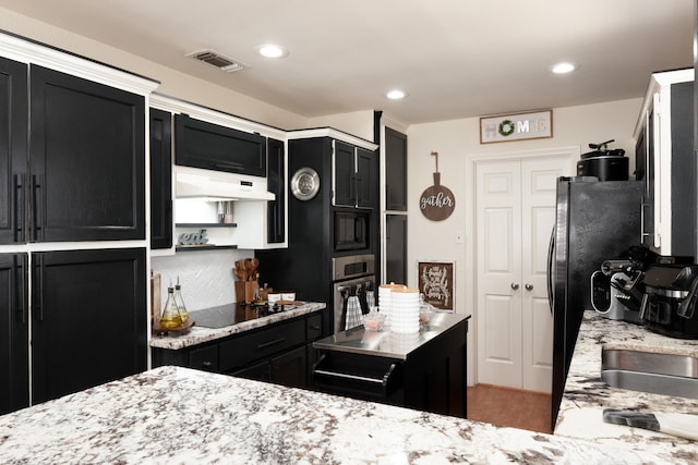 kitchen featuring light stone counters, visible vents, dark cabinetry, under cabinet range hood, and black appliances