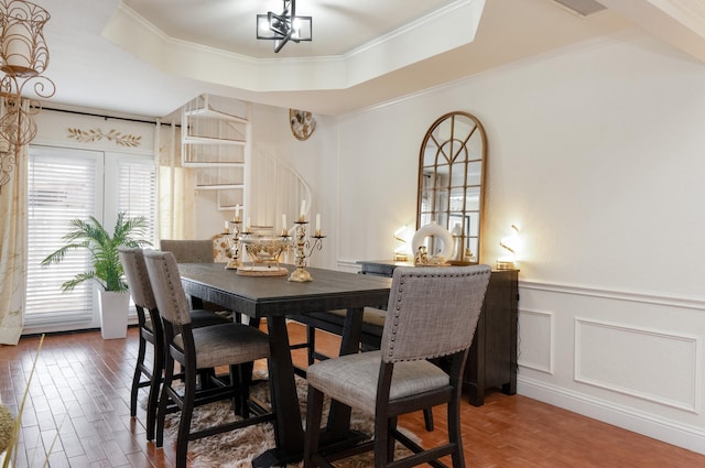 dining space featuring a wainscoted wall, wood finished floors, a raised ceiling, and a decorative wall