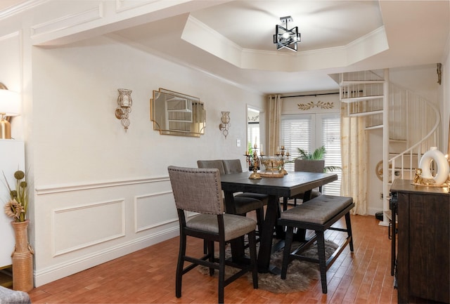 dining room featuring ornamental molding, a tray ceiling, a decorative wall, and wood finished floors