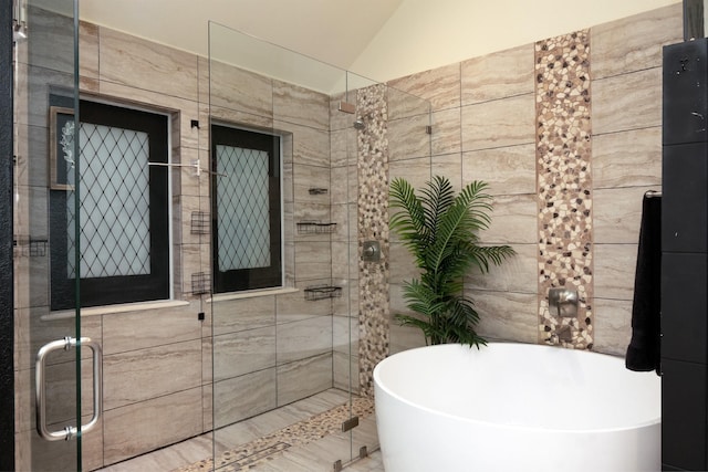 bathroom with a freestanding bath, a shower stall, tile walls, and lofted ceiling