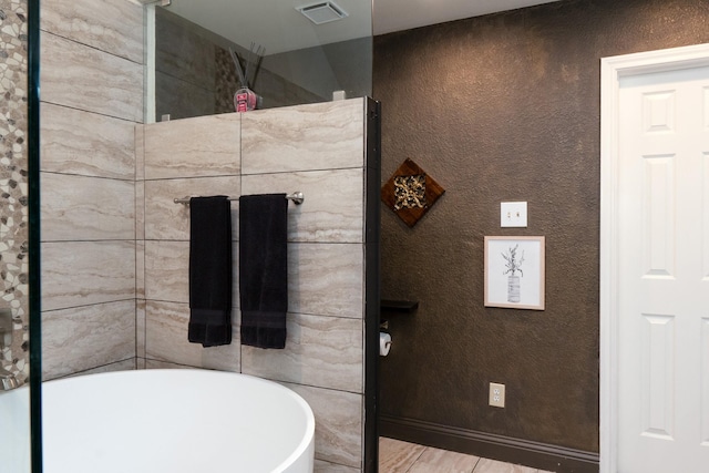 bathroom with baseboards, visible vents, a textured wall, a soaking tub, and wood finished floors