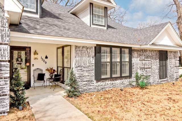 property entrance with a shingled roof and brick siding