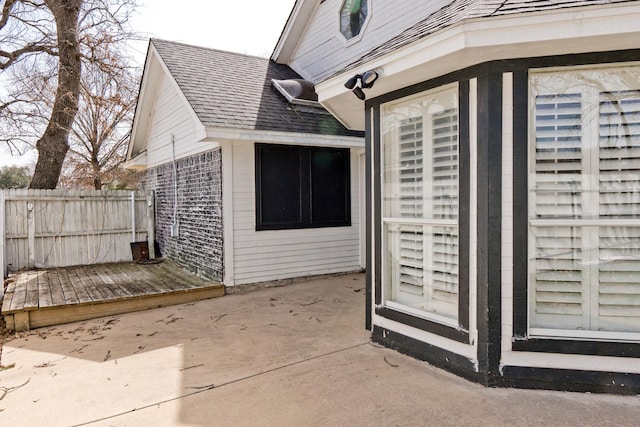 exterior space featuring a shingled roof, brick siding, fence, and a patio