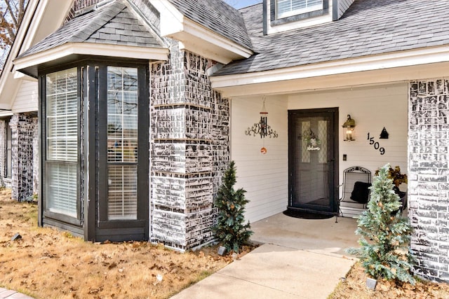 property entrance with a shingled roof and brick siding