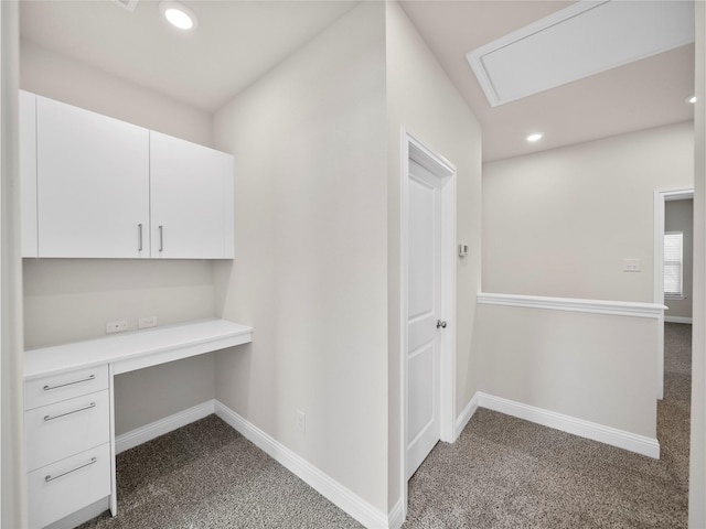 unfurnished office with dark colored carpet, built in desk, and baseboards