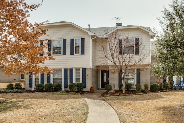 view of front of house featuring brick siding, a chimney, and a front yard