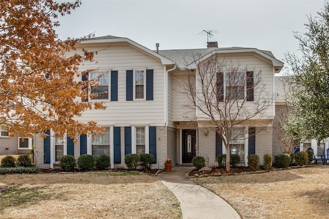 view of front of house with brick siding, a chimney, and a front yard