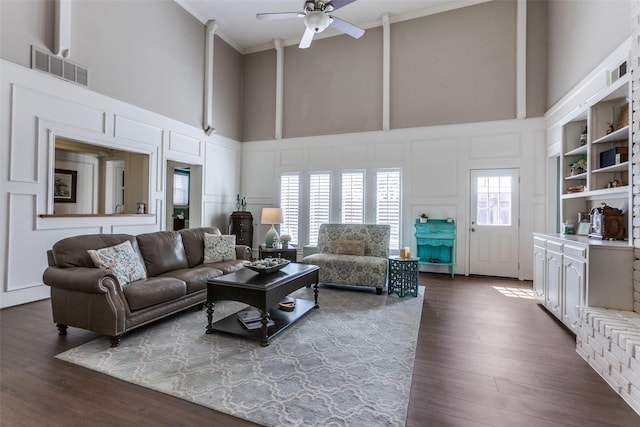 living room featuring visible vents, dark wood-style floors, a high ceiling, crown molding, and a decorative wall