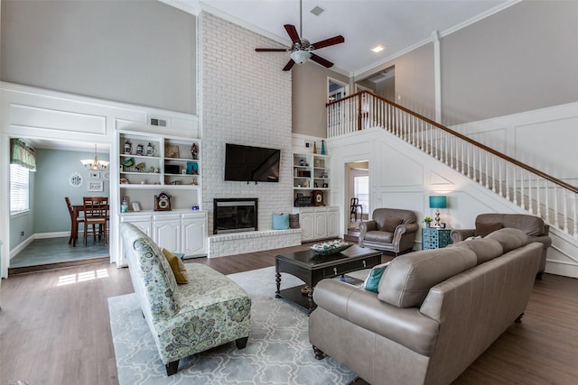 living area with stairs, crown molding, a brick fireplace, built in shelves, and a decorative wall