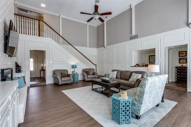 living area featuring a decorative wall, a high ceiling, a ceiling fan, crown molding, and stairway