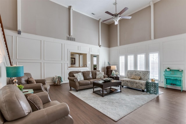 living room featuring a decorative wall, a towering ceiling, crown molding, ceiling fan, and wood finished floors
