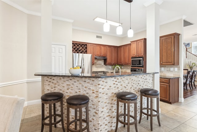 kitchen with visible vents, stainless steel appliances, crown molding, under cabinet range hood, and a kitchen bar