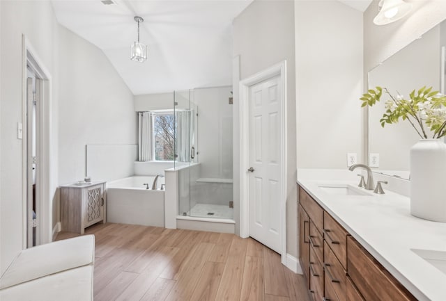 bathroom featuring double vanity, a stall shower, wood finished floors, a garden tub, and a sink