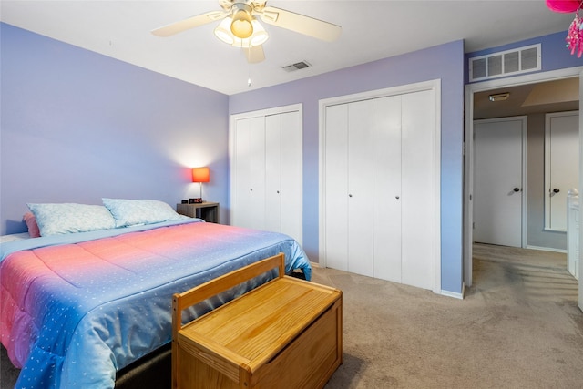 bedroom with carpet, two closets, visible vents, and a ceiling fan