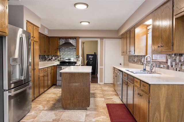 kitchen with stainless steel appliances, light countertops, a sink, wall chimney range hood, and a kitchen island