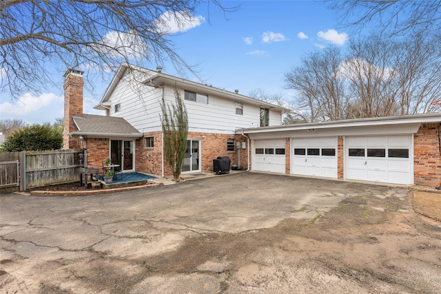 back of property featuring a garage, fence, aphalt driveway, and brick siding