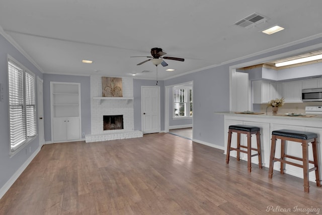 unfurnished living room featuring built in shelves, crown molding, visible vents, a brick fireplace, and wood finished floors