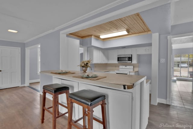 kitchen featuring range with electric cooktop, stainless steel microwave, ornamental molding, light countertops, and white cabinetry
