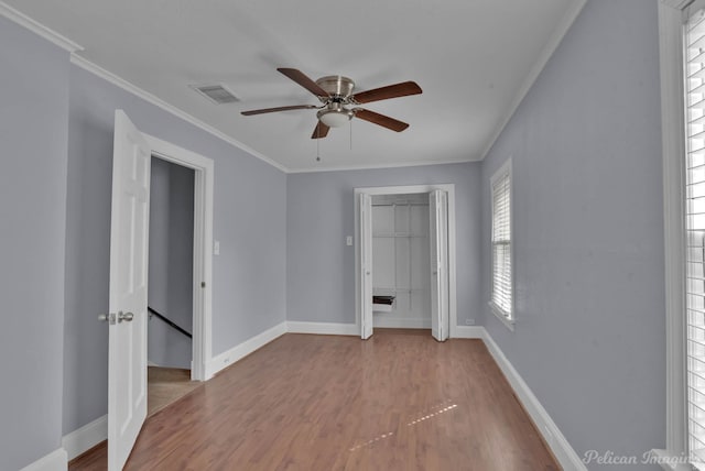 empty room featuring visible vents, crown molding, baseboards, and wood finished floors