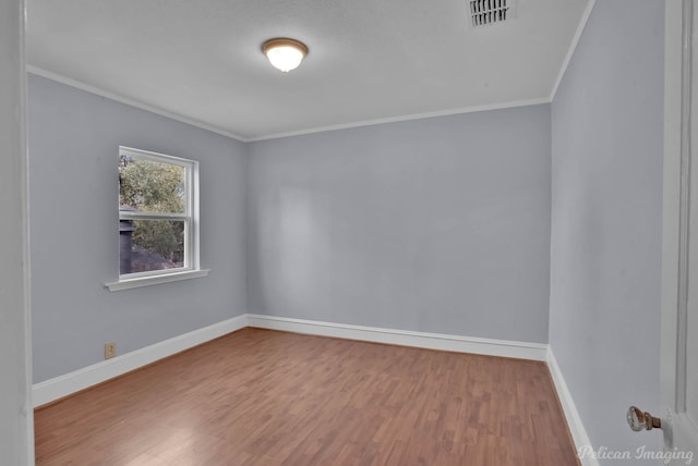empty room with crown molding, wood finished floors, visible vents, and baseboards