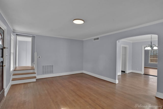 spare room with arched walkways, a wealth of natural light, wood finished floors, and visible vents