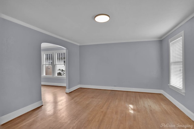 spare room featuring ornamental molding, arched walkways, baseboards, and wood finished floors