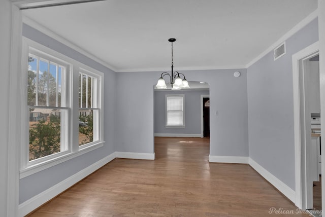unfurnished dining area with a notable chandelier, visible vents, ornamental molding, wood finished floors, and baseboards