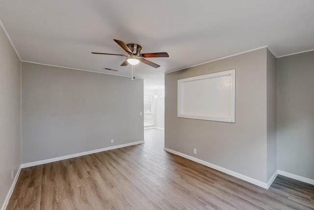 empty room featuring baseboards, visible vents, a ceiling fan, wood finished floors, and crown molding