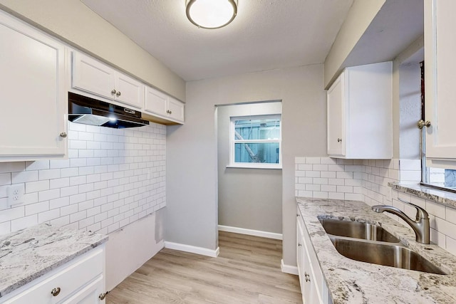 kitchen featuring under cabinet range hood, light stone counters, white cabinets, and a sink