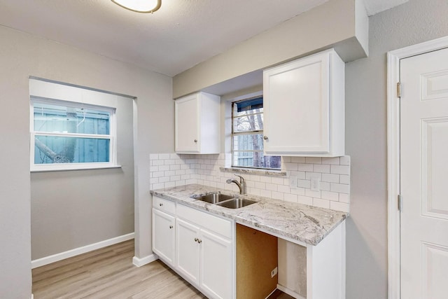 kitchen featuring light stone counters, white cabinetry, decorative backsplash, and a sink