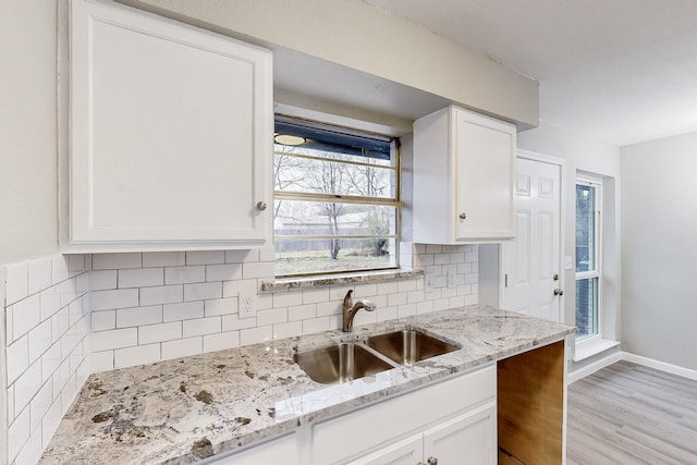 kitchen with light stone counters, tasteful backsplash, white cabinetry, a sink, and light wood-type flooring