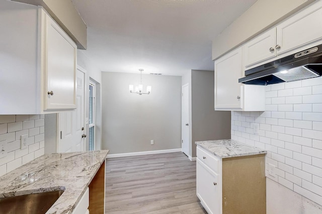 kitchen with light stone counters, white cabinets, light wood-style floors, and under cabinet range hood