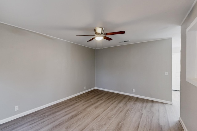 spare room featuring a ceiling fan, visible vents, baseboards, and wood finished floors