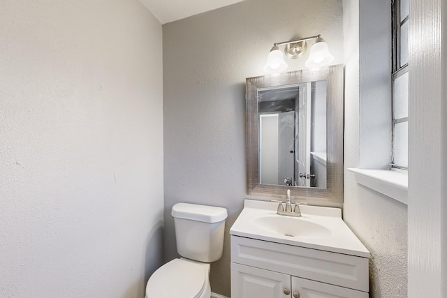 bathroom with a textured wall, vanity, and toilet