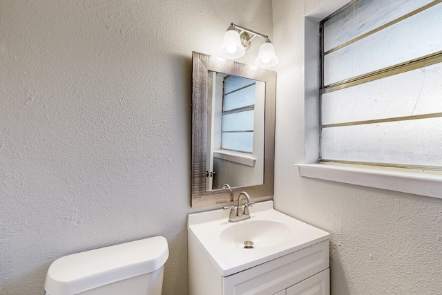 half bath with toilet, vanity, and a textured wall