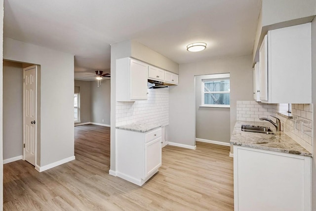 kitchen featuring white cabinetry, a sink, light wood finished floors, and light stone countertops