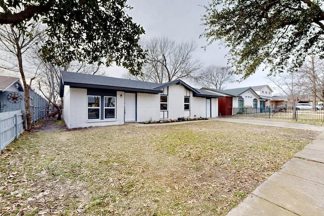 view of front of house with driveway, brick siding, a front lawn, and fence private yard