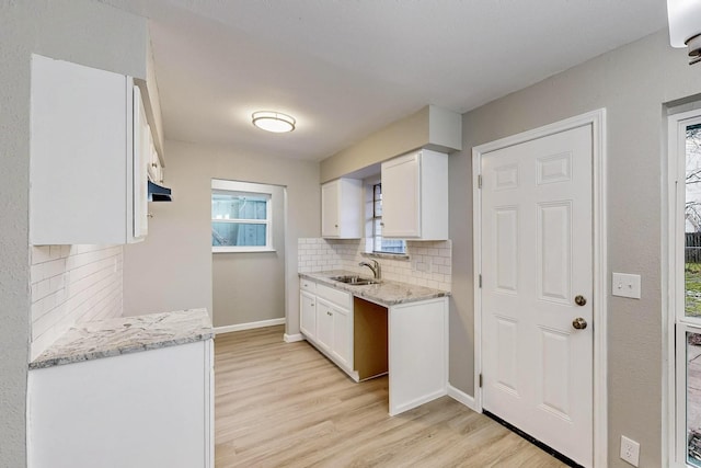 kitchen with light stone counters, light wood finished floors, decorative backsplash, white cabinets, and a sink