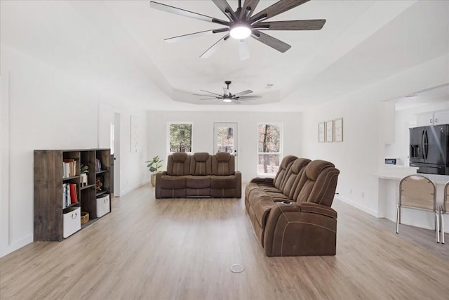 living room with a ceiling fan, light wood-type flooring, a raised ceiling, and baseboards