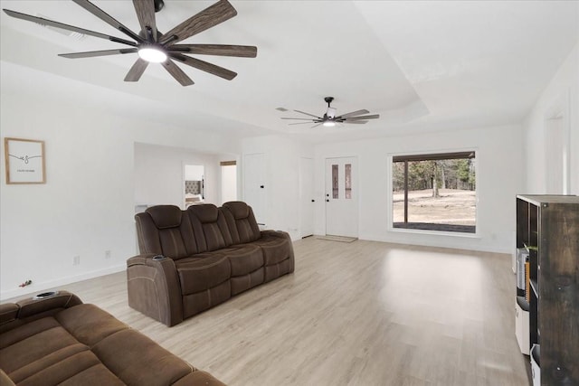 living area featuring baseboards, ceiling fan, a raised ceiling, and light wood-style floors