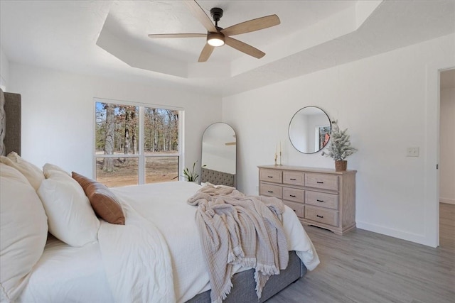 bedroom featuring light wood finished floors, ceiling fan, baseboards, and a raised ceiling