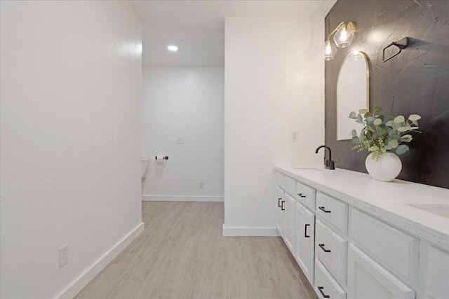 bathroom with double vanity, recessed lighting, a sink, wood finished floors, and baseboards