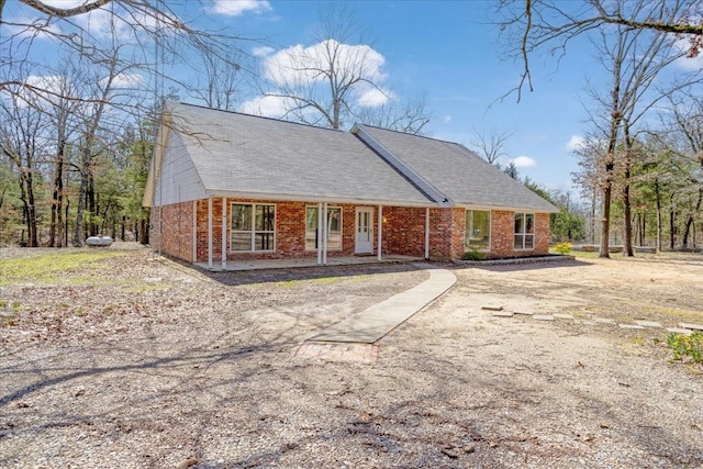 view of front of house featuring dirt driveway, brick siding, and roof with shingles