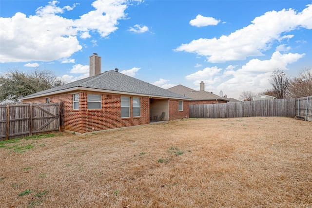 back of property featuring a chimney, brick siding, a yard, and a fenced backyard