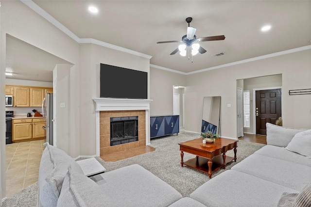 living area featuring light tile patterned floors, visible vents, ornamental molding, a ceiling fan, and a tile fireplace