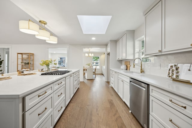 kitchen featuring a skylight, stainless steel appliances, light countertops, light wood-type flooring, and a sink