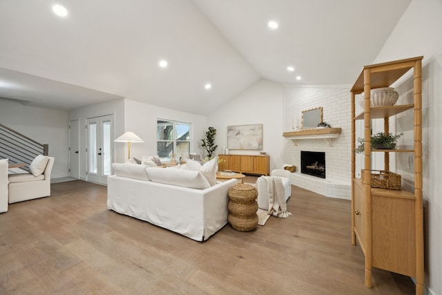 living room featuring wood finished floors, a brick fireplace, lofted ceiling, and stairs