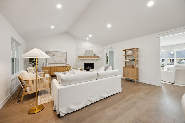 living room featuring a fireplace, vaulted ceiling, light wood-style flooring, and baseboards