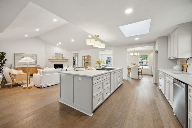 kitchen with vaulted ceiling with skylight, a fireplace, light countertops, stainless steel dishwasher, and light wood finished floors