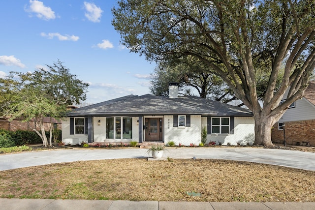 ranch-style house featuring brick siding, driveway, a chimney, and a front lawn